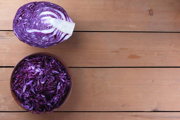 Chopped purple cabbage on a wooden background, red cabbage in a clay bowl, copy space, rustic style, vegetarian food, half fresh cabbage, minimalism