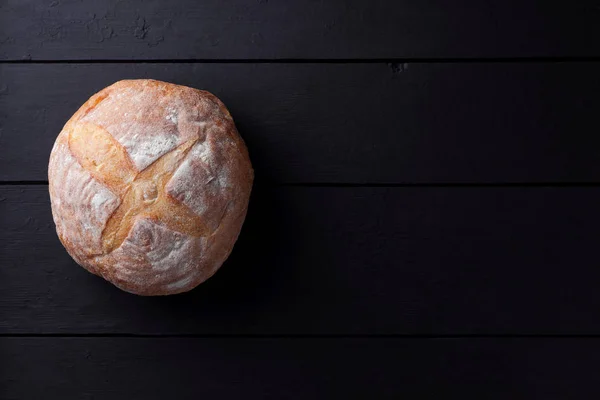 Round bread on a black background, bread from a stove on dark boards, dough for designer, copy space, rustic style, minimalism, top view, bakery, art