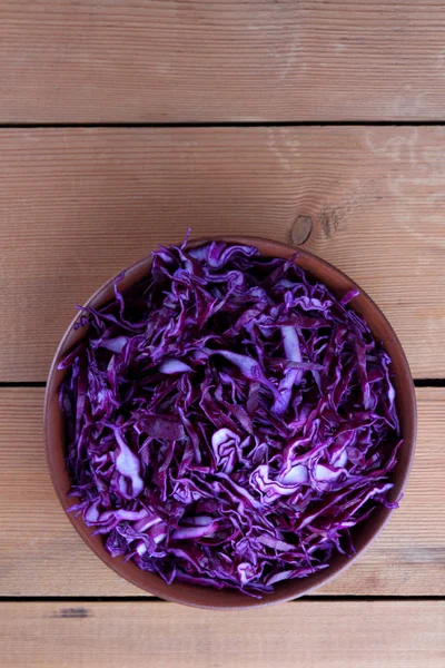 Chopped purple cabbage on a wooden background, red cabbage in a clay bowl, copy space, rustic style, vegetarian food, half fresh cabbage, minimalism, art