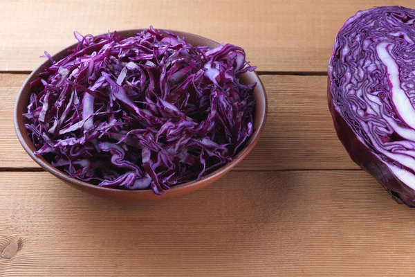 Chopped purple cabbage on a wooden background, red cabbage in a clay bowl, copy space, rustic style, vegetarian food, half fresh cabbage, minimalism, art