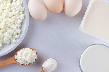 Süzme peynir, krema ve yumurta beyaz bir arka planda beyaz tahta, bir bardak süt, peynir beyaz paket, ahşap çatal bıçak takımı, rustik tarzı, çeşitli süt ürünleri alanı Kopyala
