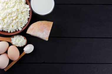 Süzme peynir ve yumurta karanlık bir arka planda çeşitli süt ürünleri karanlık panoları, bir bardak süt, bir kil plaka, ahşap çatal bıçak takımı, rustik tarzı, kopya alanı, yumuşak peynir ekmek