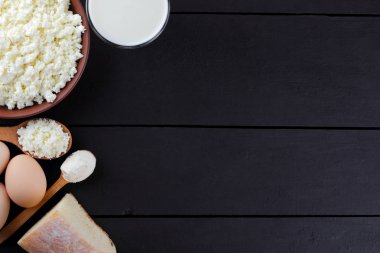 Süzme peynir ve yumurta karanlık bir arka planda çeşitli süt ürünleri karanlık panoları, bir bardak süt, bir kil plaka, ahşap çatal bıçak takımı, rustik tarzı, kopya alanı, yumuşak peynir ekmek