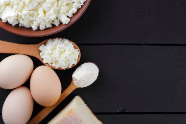 Süzme peynir ve yumurta karanlık bir arka planda çeşitli süt ürünleri karanlık panoları, bir bardak süt, bir kil plaka, ahşap çatal bıçak takımı, rustik tarzı, kopya alanı, yumuşak peynir ekmek