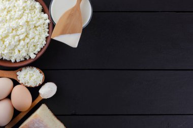 Karanlık bir arka plan üzerinde süt ve süt ürünleri ile karışık, süzme peynir ve yumurta karanlık kurullarında, bir bardak süt, bir kil plaka, ahşap çatal bıçak takımı, rustik tarzı, kopya alanı, yumuşak peynir ekmek