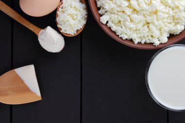 Karanlık bir arka plan üzerinde süt ve süt ürünleri ile karışık, süzme peynir ve yumurta karanlık kurullarında, bir bardak süt, bir kil plaka, ahşap çatal bıçak takımı, rustik tarzı, kopya alanı, yumuşak peynir ekmek