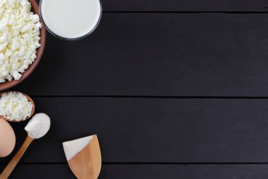 Karanlık bir arka plan üzerinde süt ve süt ürünleri ile karışık, süzme peynir ve yumurta karanlık kurullarında, bir bardak süt, bir kil plaka, ahşap çatal bıçak takımı, rustik tarzı, kopya alanı, yumuşak peynir ekmek