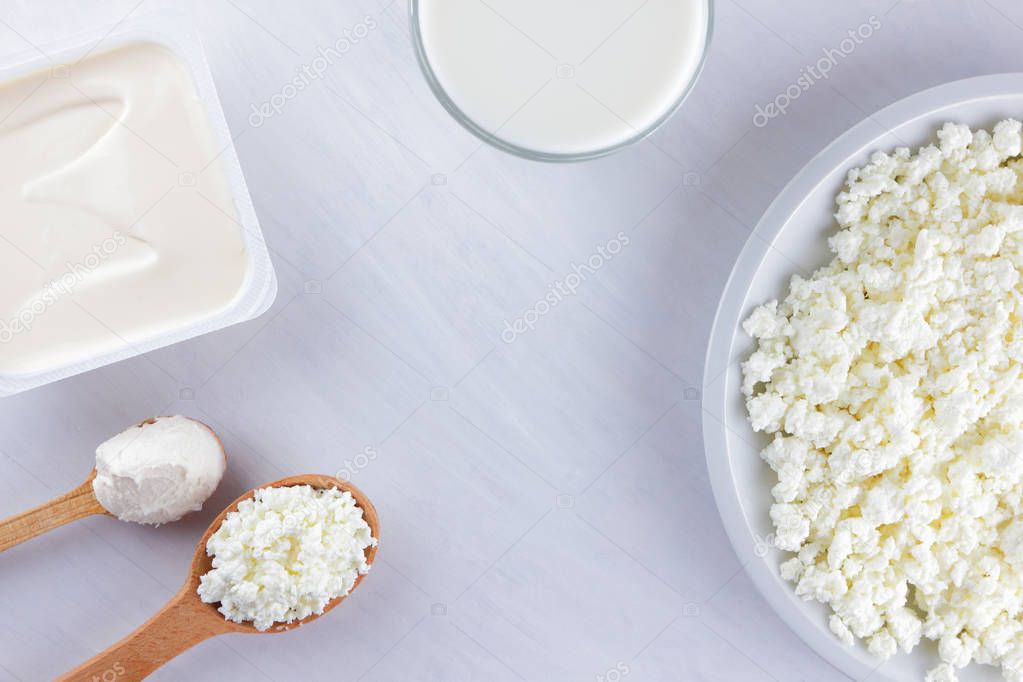 Assorted dairy products on a white board. Cottage cheese, cream and soft cheese on a white background. Milk in a glass, soft cheese for sandwiches. Wooden cutlery. Copy space. Art
