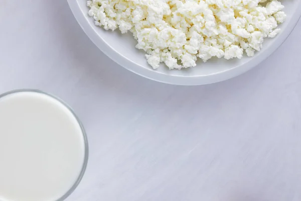 Dairy products on a white board. Cottage cheese, cream and soft cheese on a white background. Milk in a glass, soft cheese for sandwiches. Wooden cutlery. Copy space