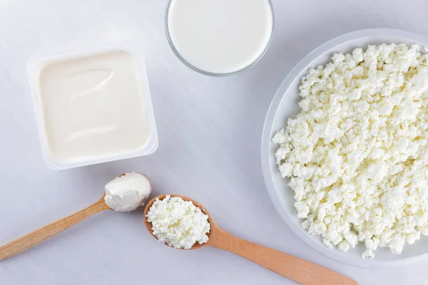 Dairy products on a white board. Cottage cheese, cream and soft cheese on a white background. Milk in a glass, soft cheese for sandwiches. Wooden cutlery. Copy space