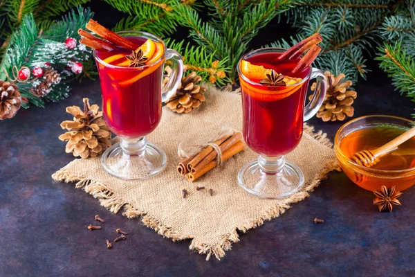 Red mulled wine and fir branches on burlap. Mulled wine with oranges, honey, cinnamon and cloves on a dark background. Hot wine with honey and spices