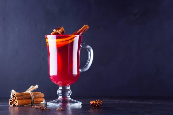Mulled wine with cinnamon sticks on dark background. Christmas mulled wine with orange, star anise and cinnamon. One glass of mulled wine and spices