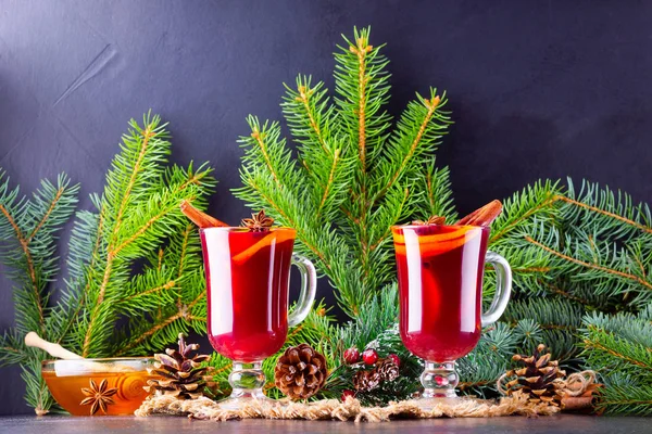 Red mulled wine and fir branches on burlap. Mulled wine with oranges, honey, cinnamon and cloves on a dark background. Hot wine with honey and spices