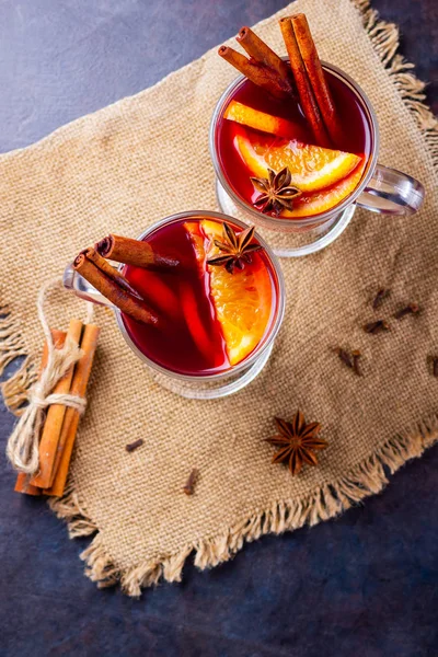 Red mulled wine on burlap. Mulled wine with oranges, cinnamon and cloves on a dark background. Hot wine with spices