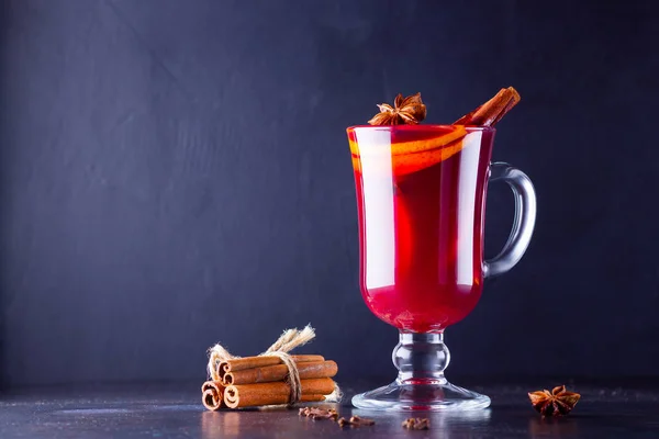 Mulled wine with cinnamon sticks on dark background. Christmas mulled wine with orange, star anise and cinnamon. One glass of mulled wine and spices