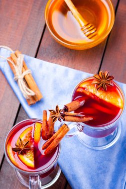 Baharatlı sıcak şarap ve ahşap zemin üzerinde bal. Noel şarabı portakallı, yıldız anason ve tarçınlı. İki bardak kırmızı şarap mavi bir peçetede.