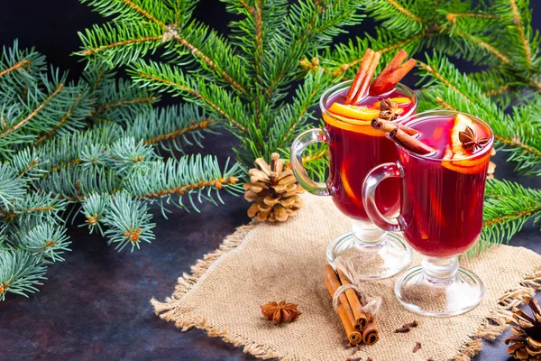 Red mulled wine and fir branches on burlap. Mulled wine with oranges, honey, cinnamon and cloves on a dark background. Hot wine with honey and spices