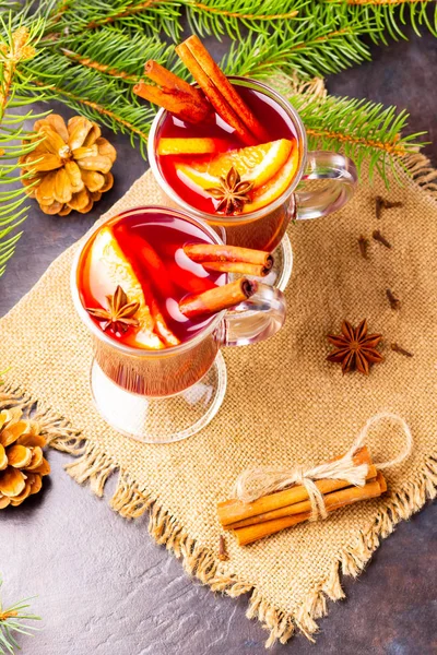 Red mulled wine and fir branches on burlap. Mulled wine with oranges, honey, cinnamon and cloves on a dark background. Hot wine with honey and spices