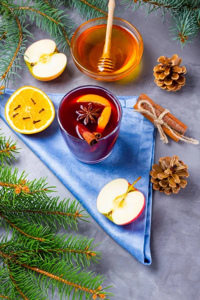 Mulled wine with spices in glass. Red mulled wine with cinnamon, anise and honey. Hot mulled wine at a cement gray background with fir branches and pine cones. Top view