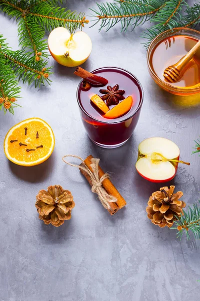Mulled wine with spices in glass. Red mulled wine with cinnamon, anise and honey. Hot mulled wine at a cement gray background with fir branches and pine cones