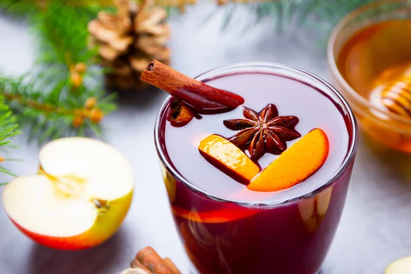 Mulled wine with spices in glass close up. Red mulled wine with cinnamon, anise and honey. Hot mulled wine at a cement gray background with fir branches and pine cones