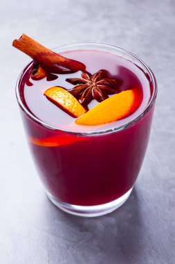 Çimento arka planında baharat olan bir bardak sıcak şarap. Noel şarabı portakallı, yıldız anason ve tarçınlı. Kırmızı şarap gri arka planda. Minimalizm. Boşluğu kopyala