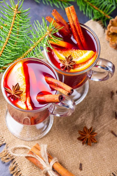 Red mulled wine and fir branches on burlap. Mulled wine with oranges, honey, cinnamon and cloves on a dark background. Hot wine with honey and spices