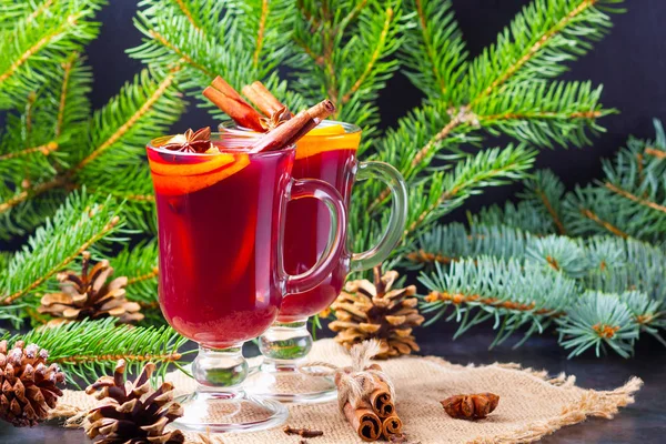 Red mulled wine and fir branches on burlap. Mulled wine with oranges, honey, cinnamon and cloves on a dark background. Hot wine with honey and spices