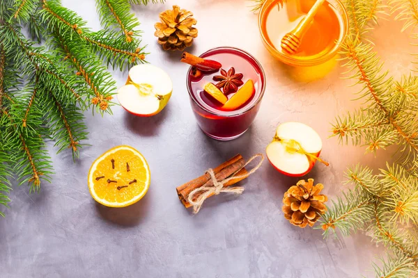 Mulled wine with spices in glass. Red mulled wine with cinnamon, anise and honey. Hot mulled wine at a cement gray background with fir branches and pine cones