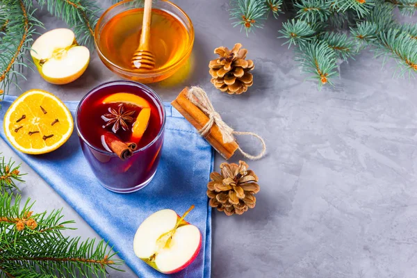 Mulled wine with spices in glass. Red mulled wine with cinnamon, anise and honey. Hot mulled wine at a cement gray background with fir branches and pine cones. Top view