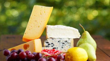Camembert peyniri, sert peynir ve üzümler ahşap tezgahta. Farklı peynir parçaları, bulanık armut ve limon. Dorblu, yumuşak peynirli ve narlı olsun. Geniş Ekran