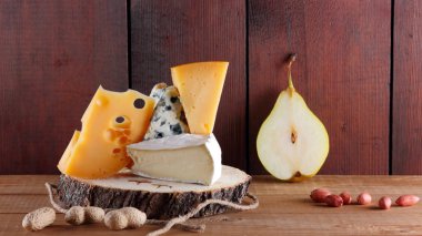 Tahta tahtalarda çeşitli peynir, armut ve fıstık çeşitleri. Camembert peyniri, sert sarı peynir, ahşap arka planda Dorblu. Süt ürünleri, armut ve fındık. Geniş Ekran