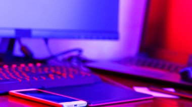 Neon ışığı altında serbest çalışan bir işyeri. Bilgisayar, grafiksel tablet ve akıllı telefon masaya. Mavi pembe ışıkta yaratıcılık için bir yer. Geniş Ekran