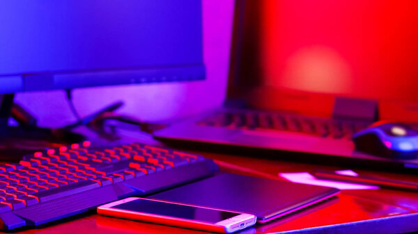 Freelancer workplace in neon light. Computer, graphics tablet and smartphone on the table. Place for creativity in blue pink light. Widescreen