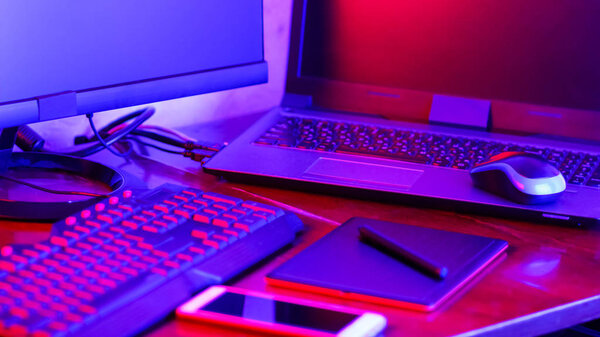 Freelancer workplace in neon light. Computer, graphics tablet and smartphone on the table. Place for creativity in blue pink light. Widescreen