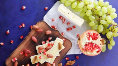 Peynir tabağı: ahşap tabakta meyve ve fındıklı peynir çeşitleri. Farklı peynir türleri. Klasik mavi arka planda Camembert, üzüm ve nar. Üst görünüm