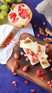 Peynir tabağı: ahşap tabakta meyve ve fındıklı peynir çeşitleri. Farklı peynir türleri. Klasik mavi arka planda Camembert, üzüm ve nar. Üst görünüm