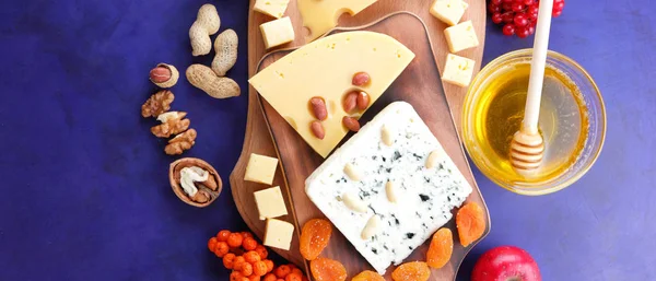 Cheese platter: variety of cheeses on wooden plate with fruits and nuts. Different types of cheese and honey. Hard cheese and berries on a classic blue background. Top view