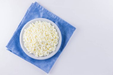 Beyaz tabakta süzme peynir. Beyaz arka planda taze süzme peynir. Minimalist tarzda mavi bir peçeteye ev yapımı kaymak. Üst Manzara. Boşluğu kopyala