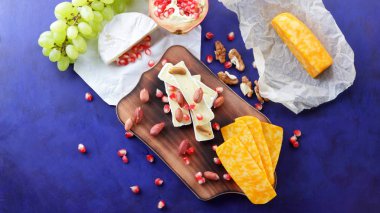 Peynir tabağı: ahşap tabakta meyve ve fındıklı peynir çeşitleri. Farklı peynir türleri. Klasik mavi arka planda Camembert, üzüm ve nar.