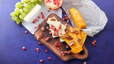 Peynir tabağı: ahşap tabakta meyve ve fındıklı peynir çeşitleri. Farklı peynir türleri. Klasik mavi arka planda Camembert, üzüm ve nar.