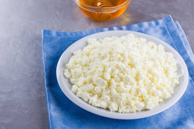 Süzme peynir ve bal. Gri arka planda taze süzme peynir. Çimento arka planında mavi bir peçeteye ev yapımı kaymak. Üst Manzara. Boşluğu kopyala