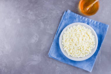 Süzme peynir ve bal. Gri arka planda taze süzme peynir. Çimento arka planında mavi bir peçeteye ev yapımı kaymak. Üst Manzara. Boşluğu kopyala