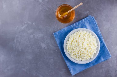 Süzme peynir ve bal. Gri arka planda taze süzme peynir. Çimento arka planında mavi bir peçeteye ev yapımı kaymak. Üst Manzara. Boşluğu kopyala