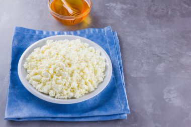 Süzme peynir ve bal. Gri arka planda taze süzme peynir. Çimento arka planında mavi bir peçeteye ev yapımı kaymak. Üst Manzara. Boşluğu kopyala