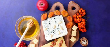 Peynir tabağı: ahşap tabakta meyve ve fındıklı peynir çeşitleri. Farklı tipte peynir ve bal. Klasik mavi arka planda sert peynir ve böğürtlen. Üst görünüm