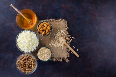Çuval bezinde sağlıklı bir diyet kahvaltısı. Sağlıklı bir kahvaltı için malzemeler - yulaf ezmesi, granola, bal, badem, süzme peynir. Koyu arkaplanda ev yapımı granola. Kırsal biçim