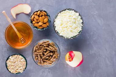 Sağlıklı diyet kahvaltısı. Sağlıklı bir kahvaltı için gerekenler: yulaf ezmesi, granola, bal, badem, elma, süzme peynir. Gri arka planda ev yapımı granola. Üst görünüm