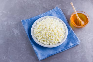 Süzme peynir ve bal. Gri arka planda taze süzme peynir. Çimento arka planında mavi bir peçeteye ev yapımı kaymak. Üst Manzara. Boşluğu kopyala