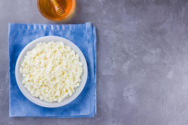 Süzme peynir ve bal. Gri arka planda taze süzme peynir. Çimento arka planında mavi bir peçeteye ev yapımı kaymak. Üst Manzara. Boşluğu kopyala